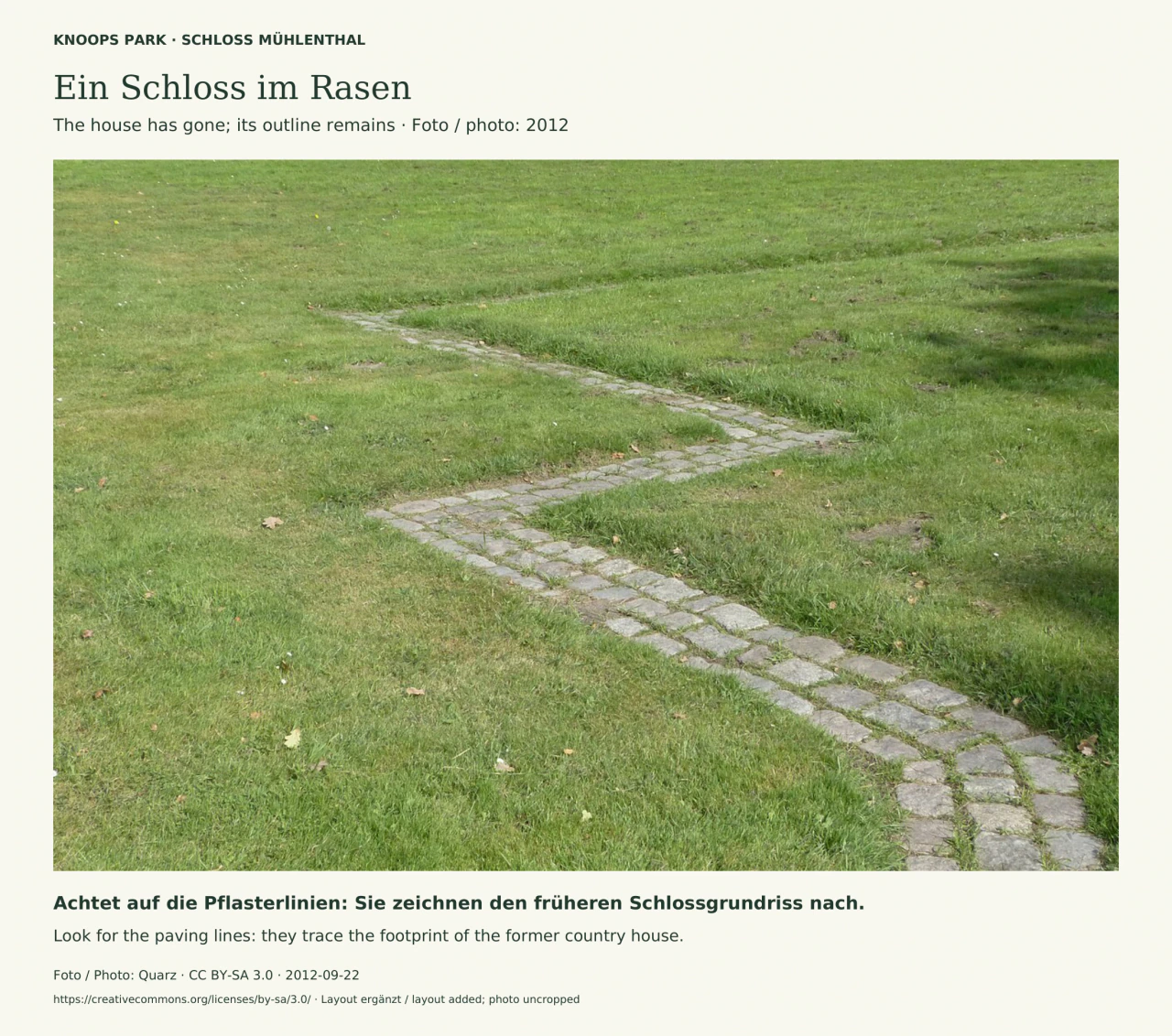 Nahaufnahme einer grünen Rasenfläche in Knoops Park. Schmale graue Pflasterstreifen verlaufen in Winkeln und einem Bogen durch das Gras und markieren einen Teil des früheren Schlossgrundrisses.