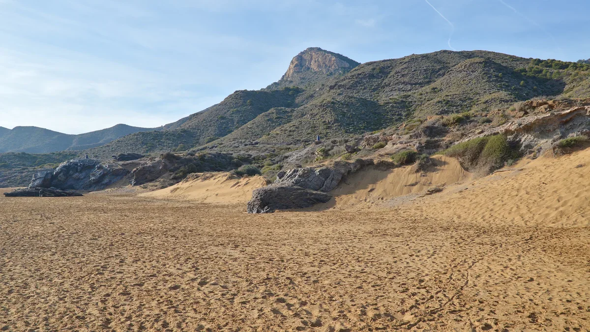 A broad sandy beach below rocky outcrops and scrub-covered hills in Calblanque.