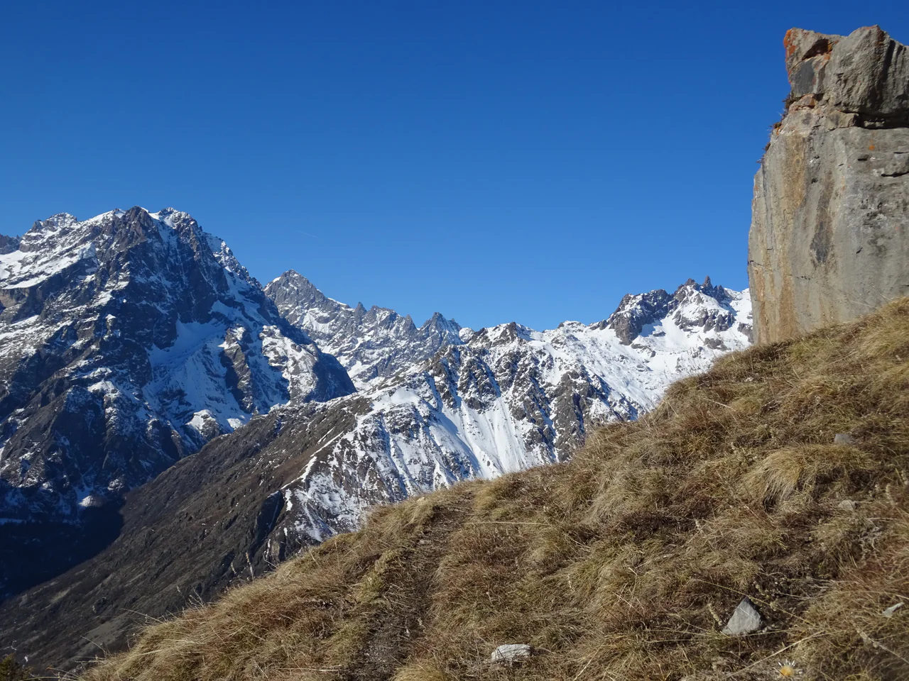 Snow-streaked jagged mountains behind a dry grassy slope, with a large weathered concrete structure at the far right edge.