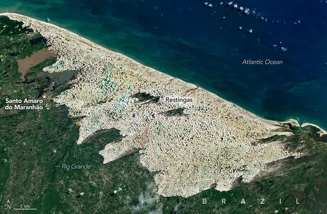 A NASA-processed Landsat 9 satellite image shows a broad white coastal dune field threaded with blue-green lagoons, dark green vegetation along its margins and islands, and the blue Atlantic Ocean. Source labels identify the Atlantic Ocean, Santo Amaro do Maranhão, restingas, Rio Grande and Brazil; a north arrow and scale remain visible. These source annotations are not visitor-navigation instructions.