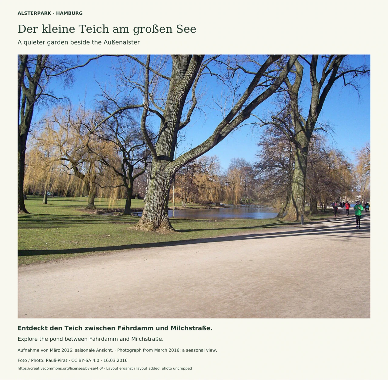 Ein breiter heller Weg führt im Vordergrund an großen, noch kahlen Bäumen vorbei. Hinter den Stämmen liegen Rasen und ein kleiner Teich; rechts laufen mehrere Menschen den Weg entlang. Blauer Himmel und lange Baumschatten prägen die Märzaufnahme. Zweisprachiger Titel, Bildhinweis und Credit rahmen das Foto.