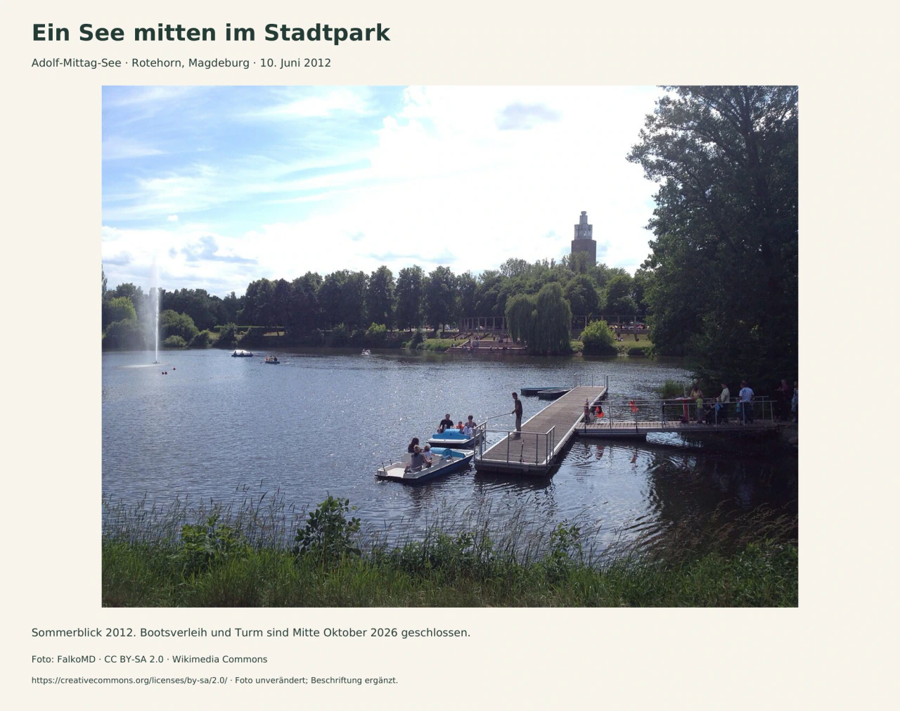 Blick über einen See mit Fontäne, mehreren Booten und einem Bootssteg mit Besuchern am rechten Ufer. Hinter der gegenüberliegenden Baumreihe ragt der Albinmüller-Turm hervor.