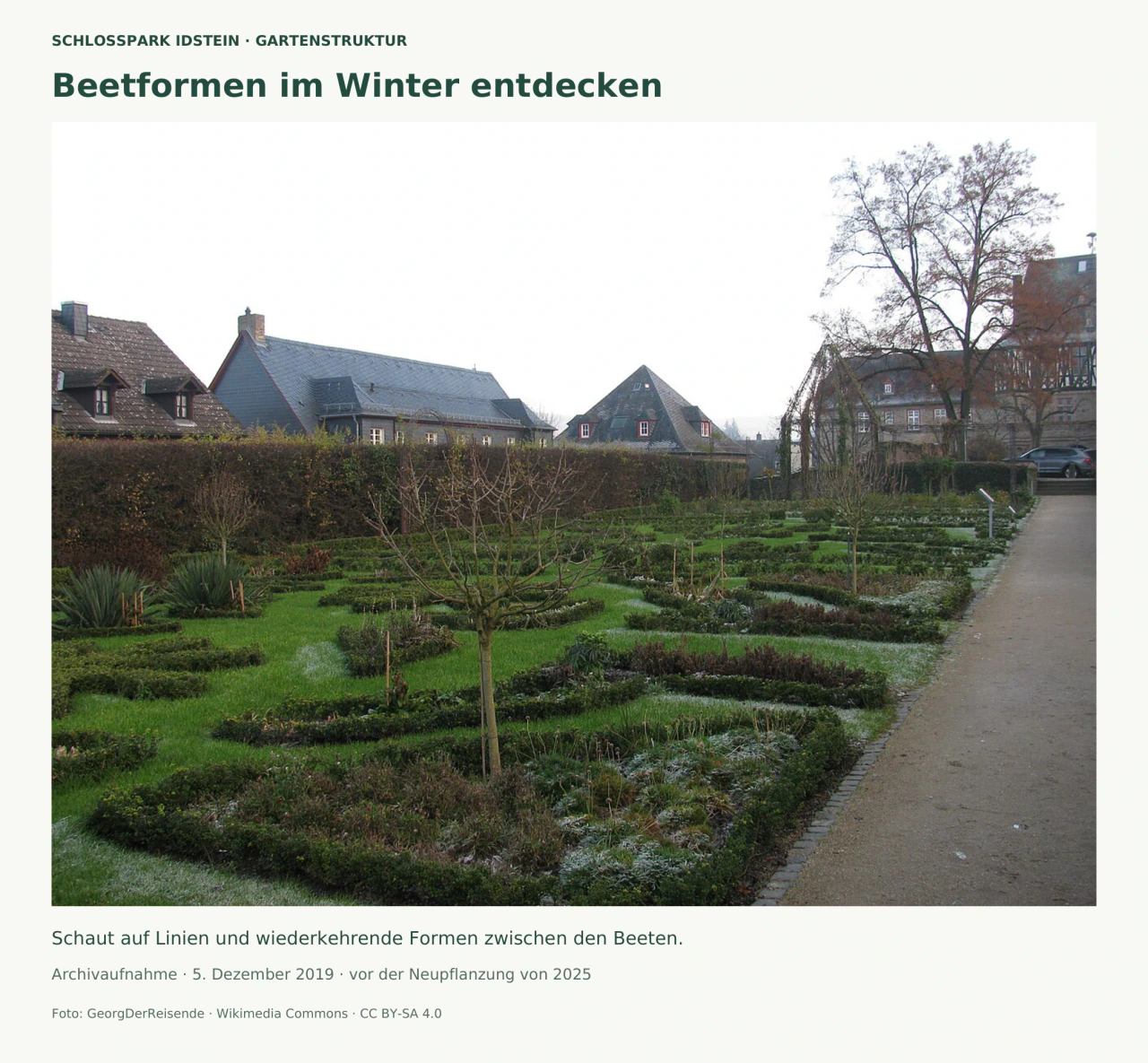 Winterfoto eines kleinen formalen Gartens: niedrige Hecken umschließen geschwungene Beete, dazwischen wachsen kahle kleine Bäume. Rechts verläuft ein gerader Weg; dahinter stehen historische Häuser.