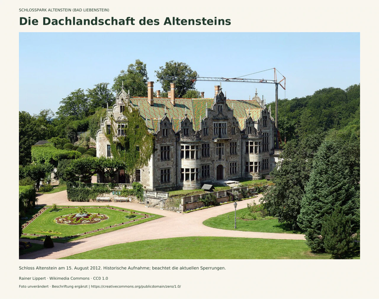Historisches Foto von Schloss Altenstein: verzierte Steingiebel, farbig gemustertes Dach und ein Baukran hinter dem Gebäude; davor Wege, Rasen und ein ornamentales Beet.