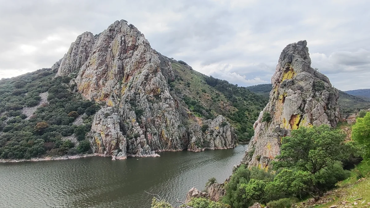Steep pale rock faces and wooded slopes rise from dark water beneath a cloudy sky at Salto del Gitano.