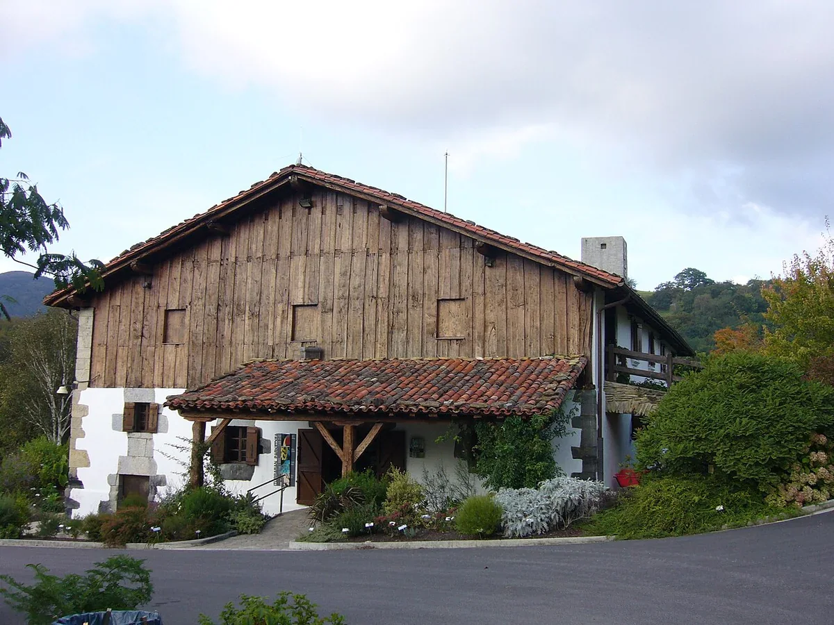 The white-walled Iturraran visitor centre has a timber gable, tiled roofs, a paved forecourt and planted borders.