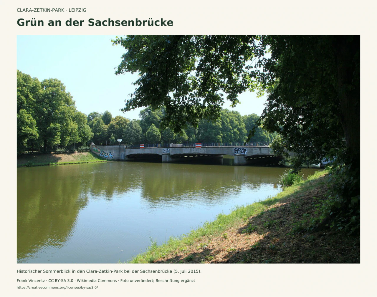 Die niedrige Sachsenbrücke über dem Elsterflutbett im Clara-Zetkin-Park, eingerahmt von grünen Bäumen und einem beschatteten Ufer; Sommeraufnahme von 2015.