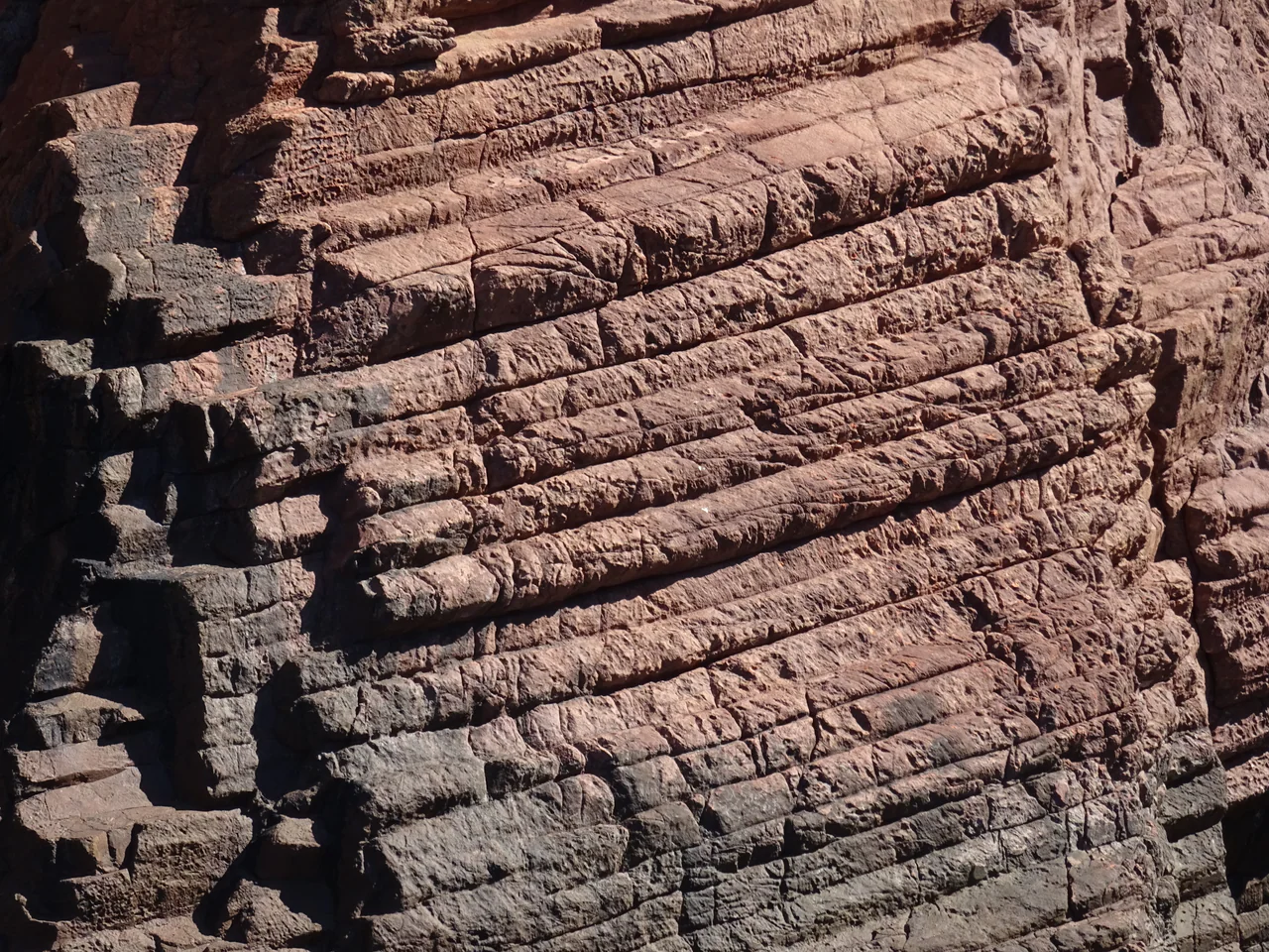 Close view of red-brown rock columns divided by diagonal cracks and dark recesses.