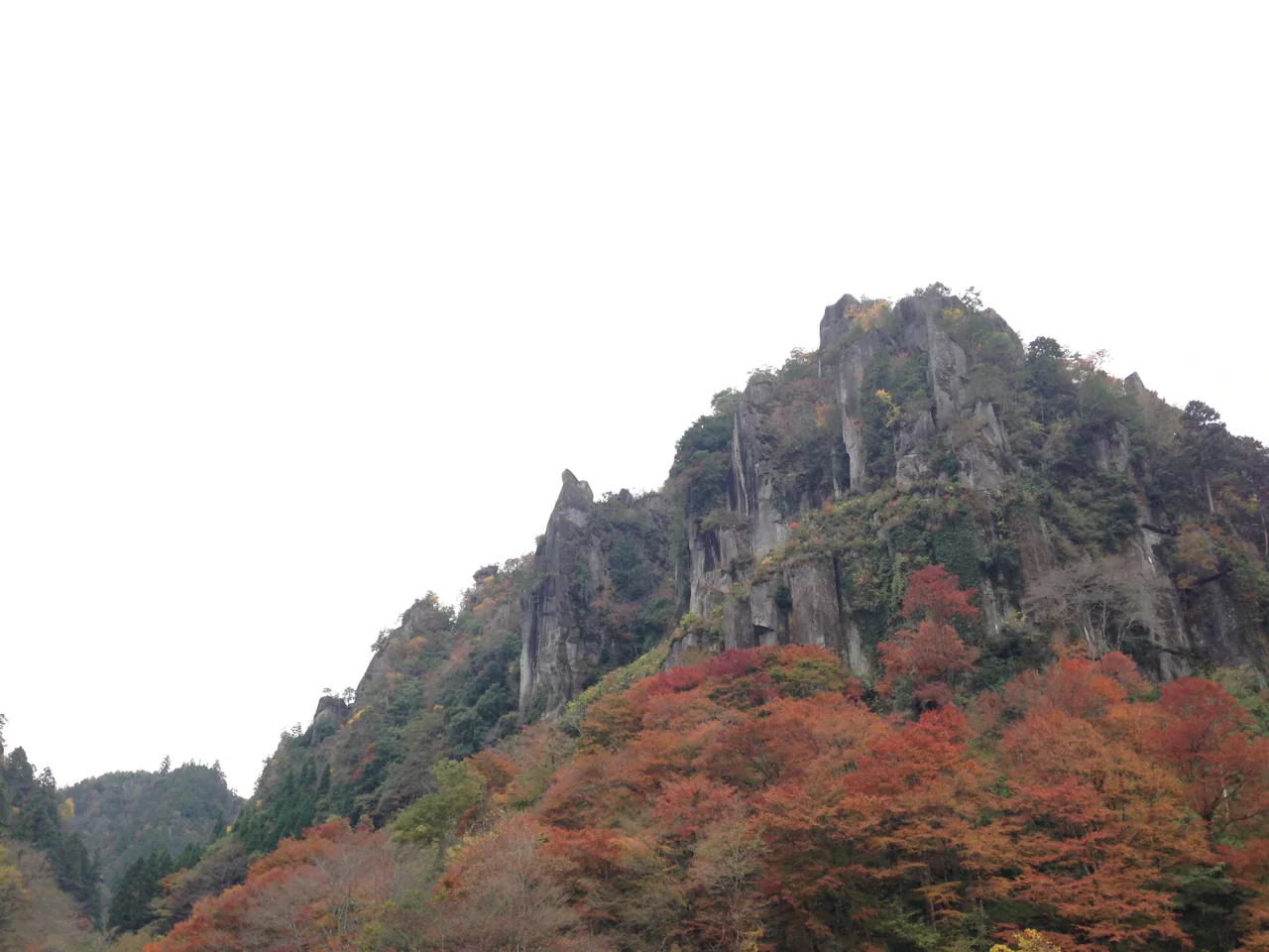A tall, jagged rock face rises above trees with green, orange and red foliage.