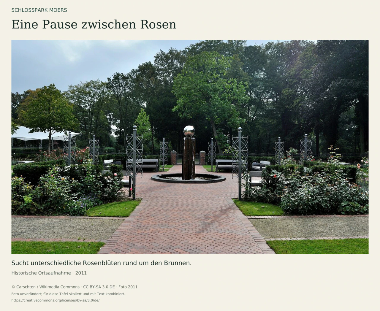 Historische Aufnahme des Rosariums im Schlosspark Moers: ein runder Brunnen mit glänzender Kugel, symmetrische Rosenbeete, Rankstützen und Bänke vor hohen Bäumen.