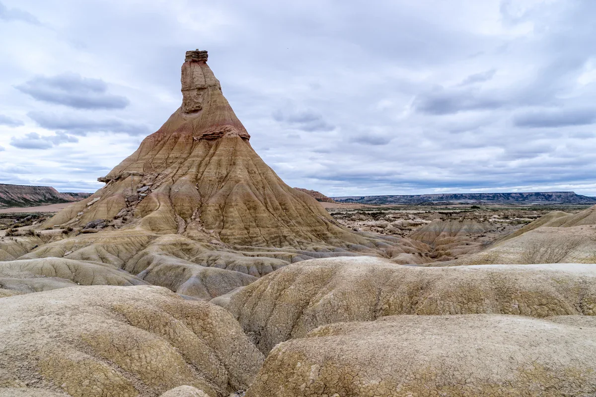 La formación de Castildetierra, que se estrecha hacia una capa superior oscura y resistente, se alza sobre un terreno claro surcado por barrancos bajo un cielo cubierto.