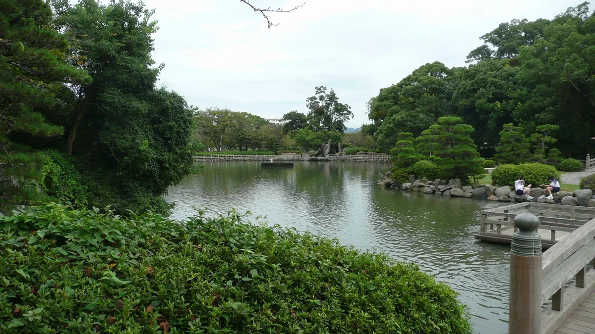 A tree-lined pond with rocks and shaped trees along its far bank; wooden railings frame the right foreground.
