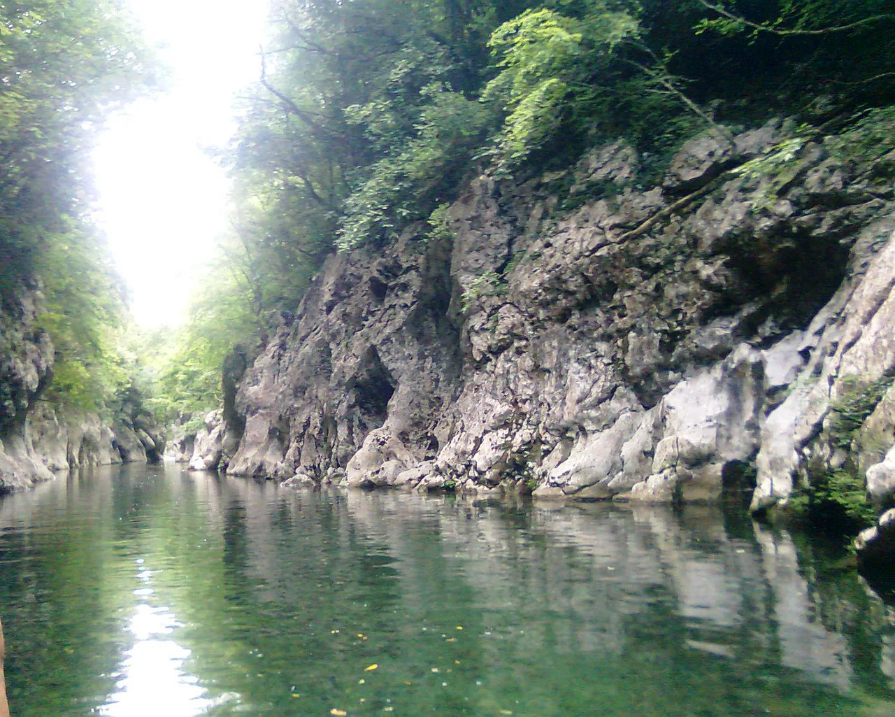 Green water between steep rock walls, with leafy trees above the narrow Calore gorge.