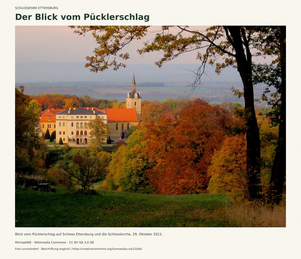 Herbstlicher Blick vom Pücklerschlag auf Schloss Ettersburg und die Kirche mit rotem Dach und hohem Turm, umrahmt von bunten Parkbäumen; im Vordergrund eine Wiese.